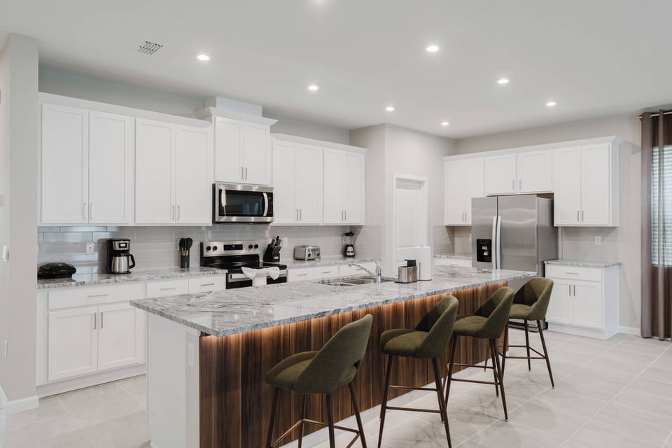 Experience a bright kitchen with elegant white cabinetry and a stunning gray and white marble island, ideal for casual dining. The warm wooden bar and stainless steel appliances ensure convenience for all your cooking endeavors.