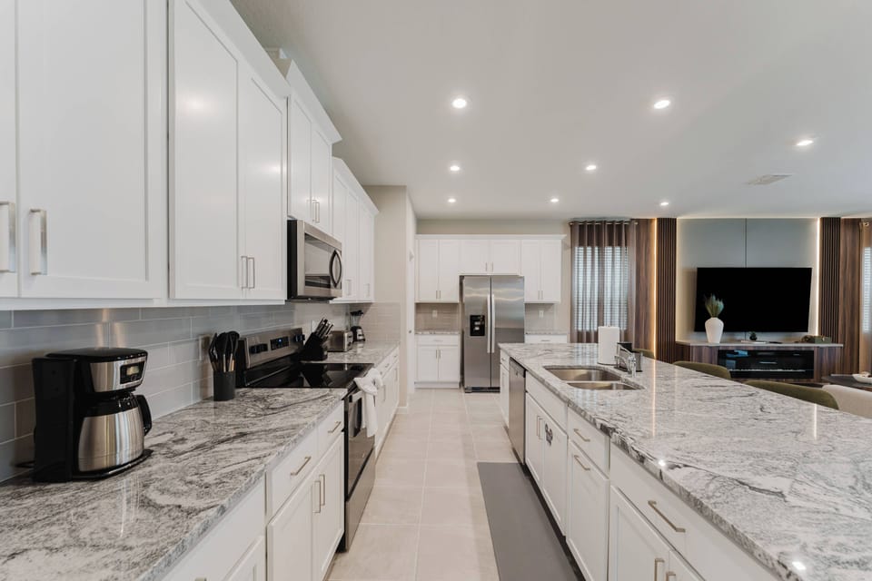 This modern kitchen features glossy white cabinets and spacious granite countertops, creating a bright space for meal prep. Equipped with stainless steel appliances and stylish lighting, it's perfect for your culinary creativity.
