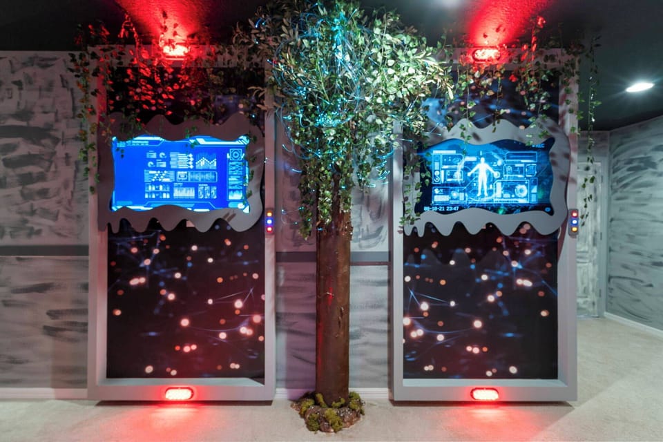 Immerse yourself in a whimsical setting with glowing blue screens and textured walls, featuring a charming faux tree and playful lighting. This unique space invites you to enjoy a fun experience like no other.