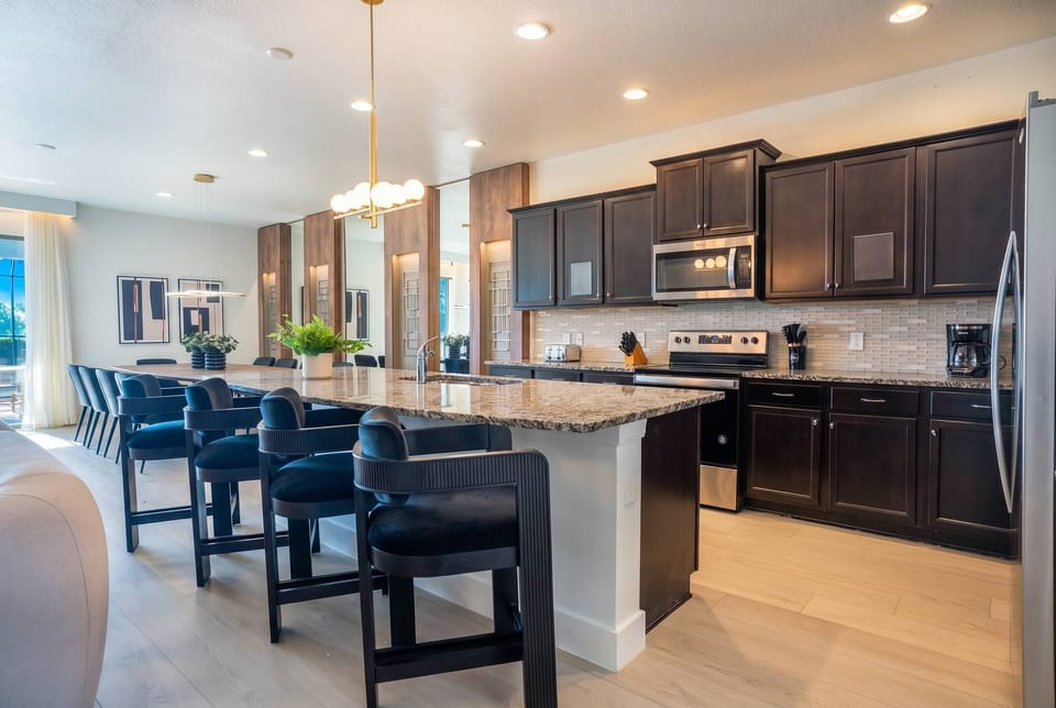 Cook and gather in a stylish kitchen with dark cabinetry, granite countertops, stainless steel appliances, a large island, black bar seating, and warm lighting, perfect for meals during your vacation.