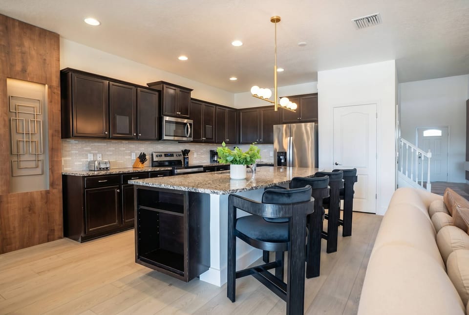 Cook and gather in a stylish kitchen with dark cabinetry, granite countertops, stainless steel appliances, a large island, black bar seating, and warm lighting, perfect for meals during your vacation.