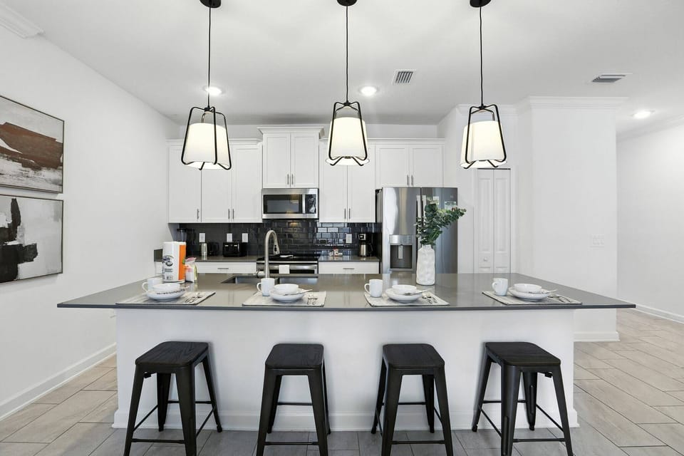 Step into a stylish kitchen featuring sleek black bar stools and illuminated by elegant pendant lights. The modern countertop complements the pristine cabinetry, creating an ideal space for cooking or casual gatherings.