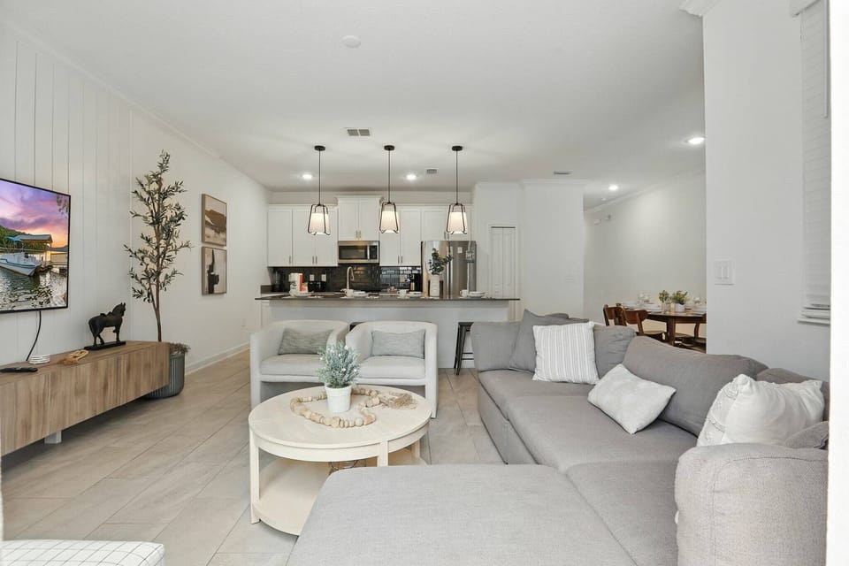Welcome to a stylish living area with a cozy gray sectional and light wood flooring. The open layout leads to a modern kitchen with sleek pendant lighting, creating a relaxing, bright space for you to enjoy.