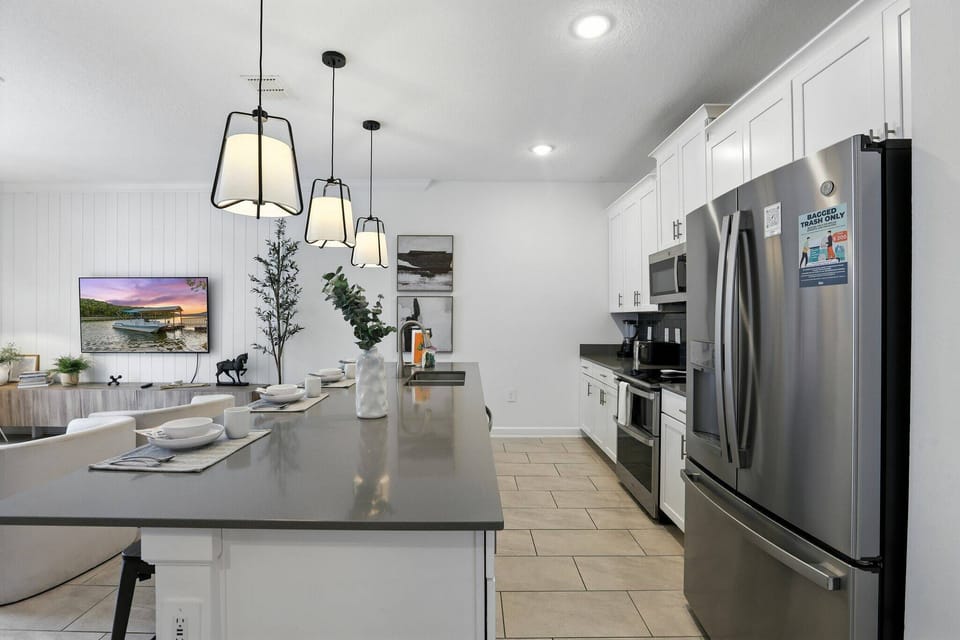 Experience a stylish kitchen with sleek stainless steel appliances and a spacious dark stone island, ideal for casual meals. The warm glow of pendant lighting creates a bright, inviting atmosphere for your culinary adventures.