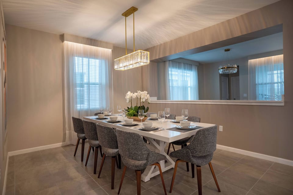 Gather at the elegant white dining table surrounded by plush gray chairs, perfect for sharing meals with loved ones. The chandelier's soft glow enhances the warm, inviting atmosphere created by the subtle wall textures.