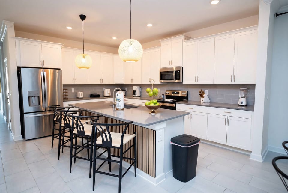 Cook and gather in a bright modern kitchen with white cabinets, stainless steel appliances, a spacious island, bar seating, warm pendant lights, and wood accents.