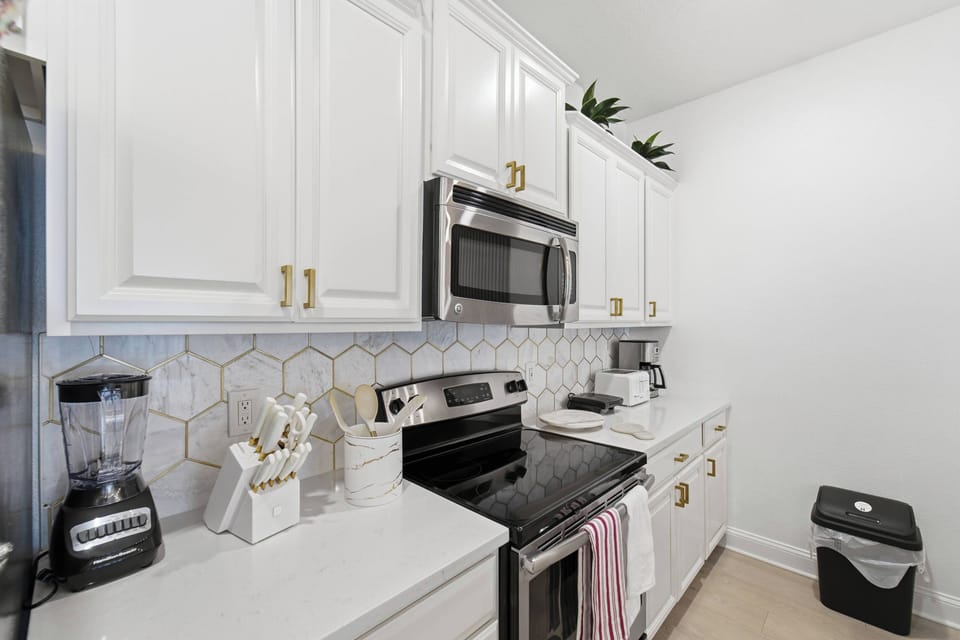 Experience the charm of this beautifully designed kitchen with sleek white cabinetry, gold hardware, and a chic hexagonal backsplash. Modern stainless steel appliances make cooking enjoyable in this inviting space.
