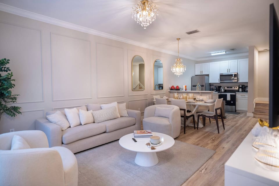 Enjoy a cozy living area with soft beige furnishings and a plush rug, perfect for relaxation. The elegant chandelier adds warmth to the dining space, seamlessly connecting to the modern kitchen for effortless entertaining.