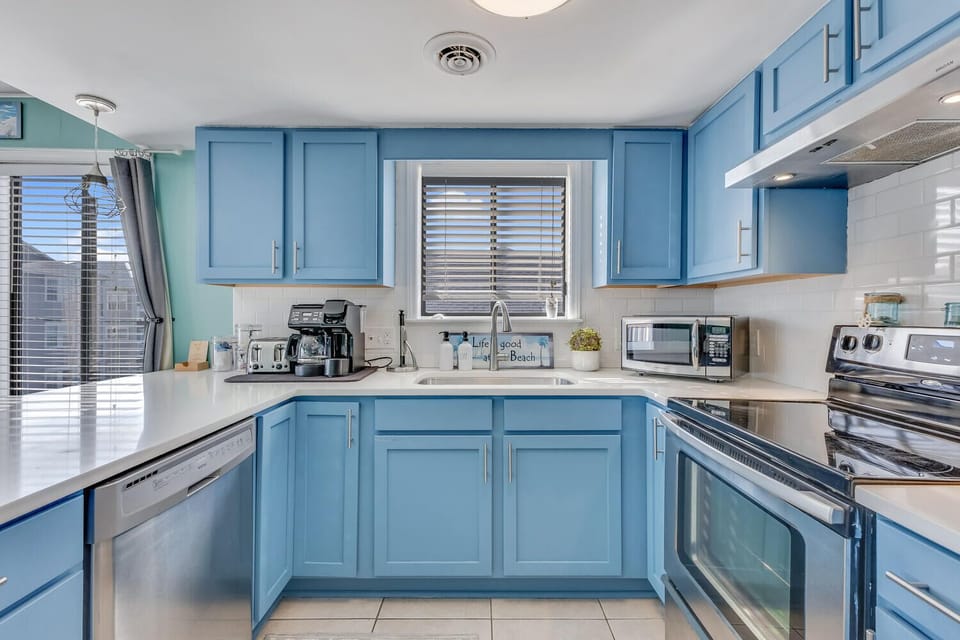 Your fully equipped kitchen awaits with beautiful blue cabinetry, stainless appliances, and coastal charm perfect for preparing beach vacation meals.