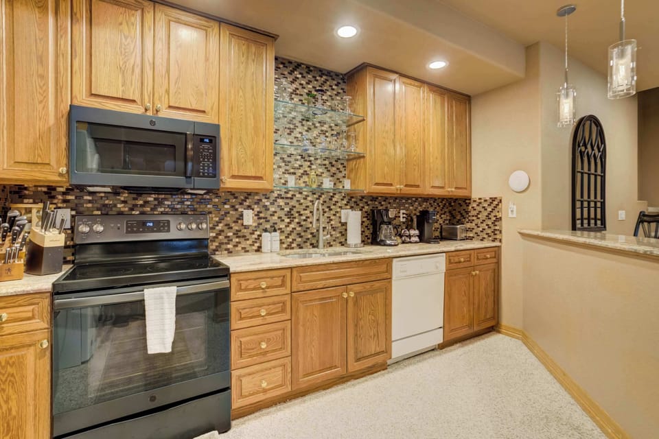 The fully equipped kitchen features professional-grade appliances, including a smooth-top range and built-in microwave. Sleek cabinetry and a decorative tile backsplash create a modern and functional space for preparing vacation meals.