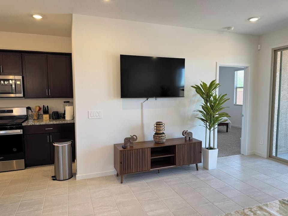 Living area with wall TV, console, plant, and kitchen view