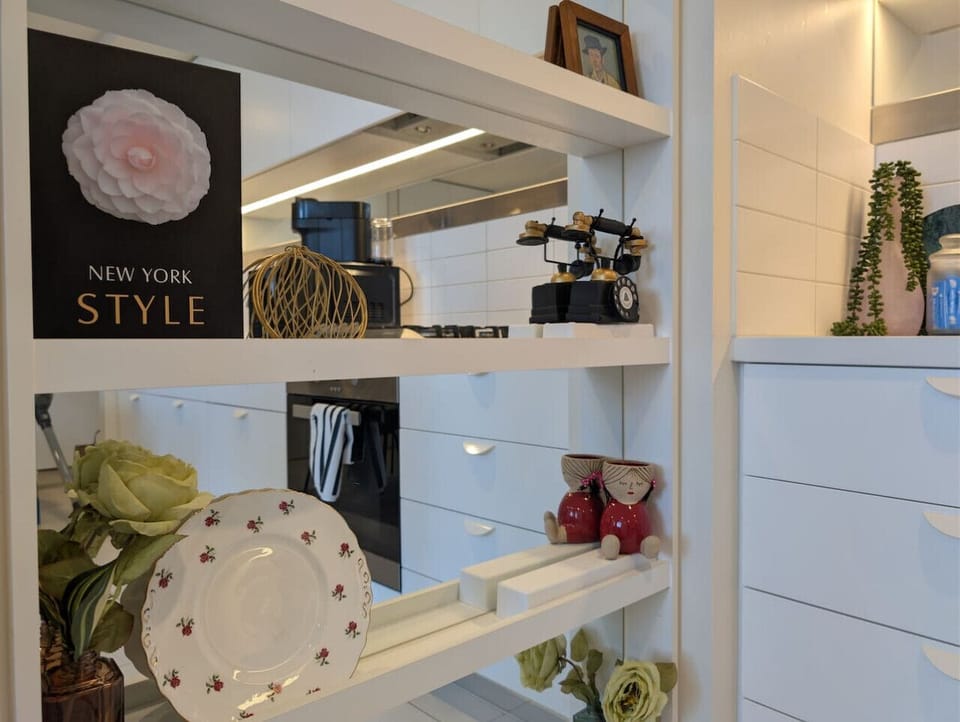 Decorative shelving between the living area and kitchen, styled with vintage ornaments, ceramic pieces, and trailing plants. These thoughtful details give the space a collected, homey character that sets it apart from a standard apartment.
