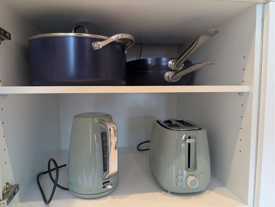Kitchen cupboard stocked with pots, pans, a kettle, and a toaster — all the basics needed to cook full meals or put together a quick breakfast during your stay.