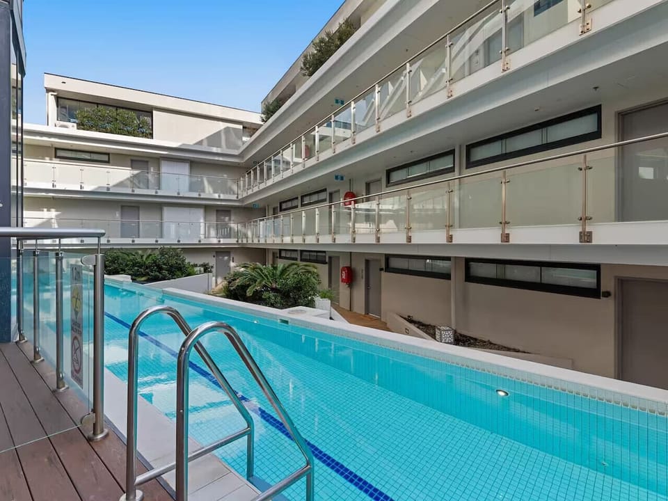 Building amenity outdoor lap pool set within a landscaped courtyard, with timber decking and glass balustrades on the surrounding levels. A clean, well-maintained space for guests to use during their stay.