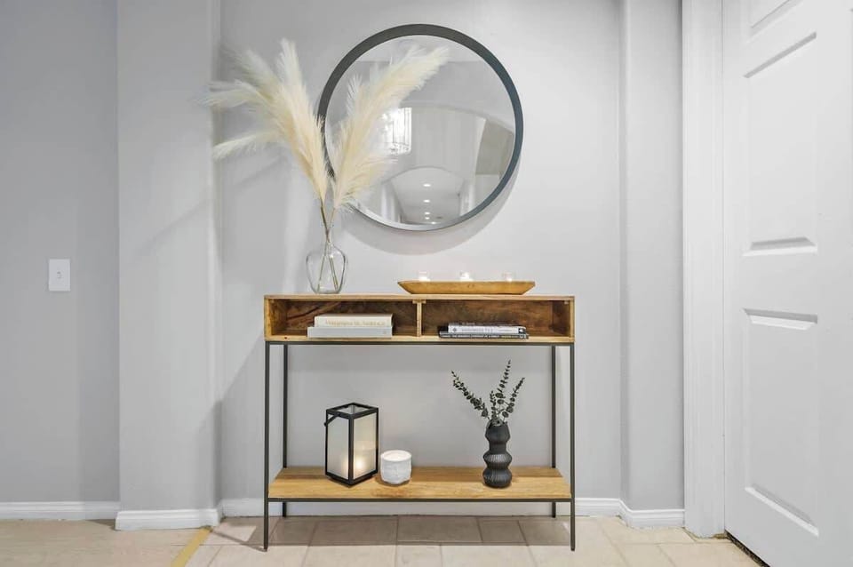 A stylish and minimal entryway featuring a wooden console table with open shelves and black metal accents. The neutral tones and clean design create a warm and inviting atmosphere.