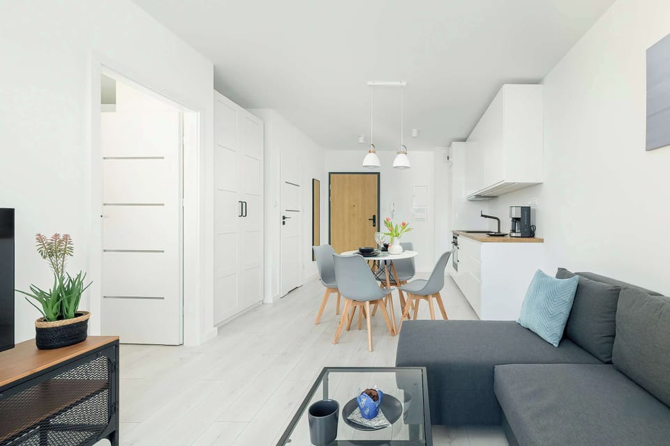 A bright living room with a grey sofa, coffee table, and floor-to-ceiling windows leading to a balcony. The space feels airy and inviting.