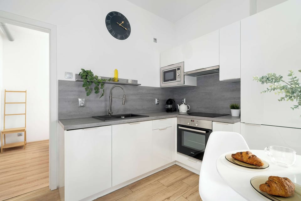 A kitchen view showing white cabinetry and a gray countertop. Built-in appliances are neatly arranged. The space feels modern and efficient.