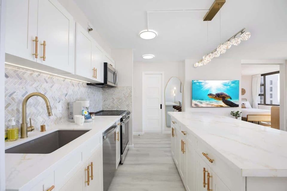 Cook with a view in this stunning, fully-equipped kitchen featuring marble-style countertops, gold accents, and a sleek herringbone backsplash.