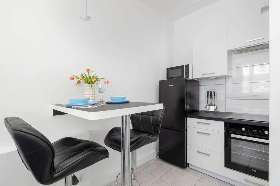 A kitchen and dining area with a small table and chairs. White cabinetry and dark countertops create a modern contrast. The space feels efficient and well organized.