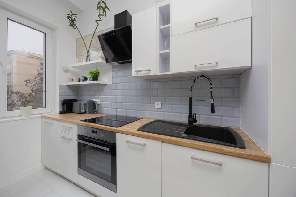 A modern kitchen with white cabinets and a wooden countertop. Built-in appliances are arranged neatly for efficient use. The design looks clean and functional.