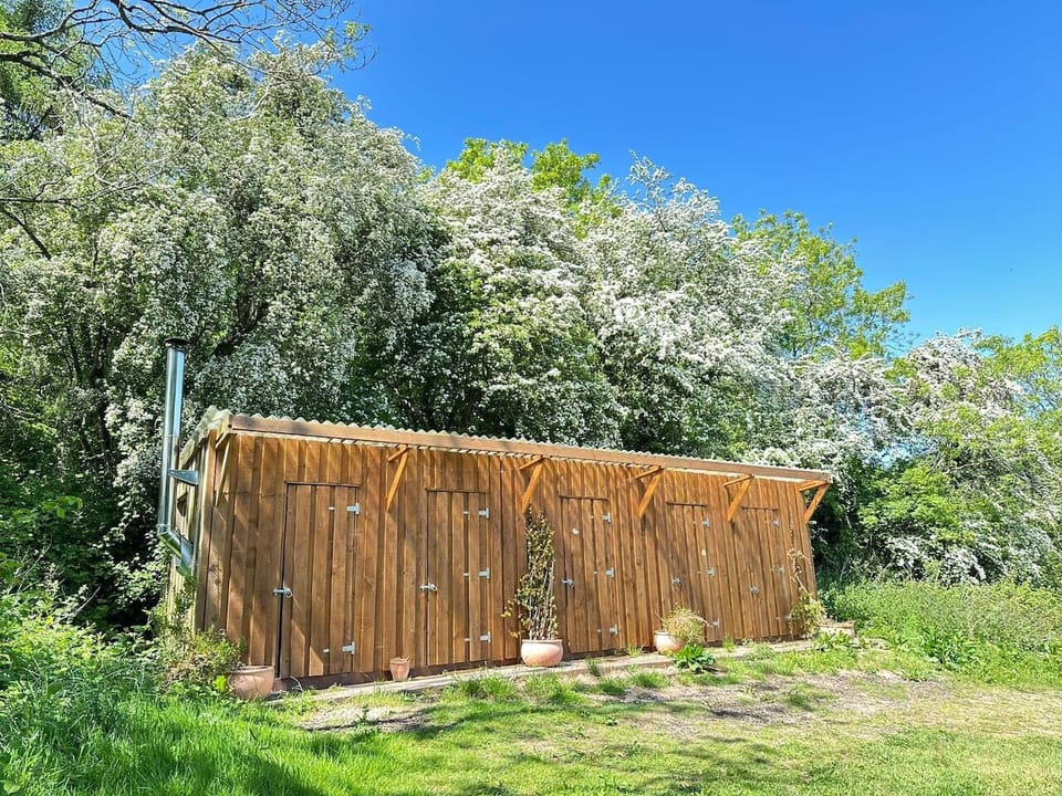 The wooden shower block building is set beside greenery and trees on a sunny day