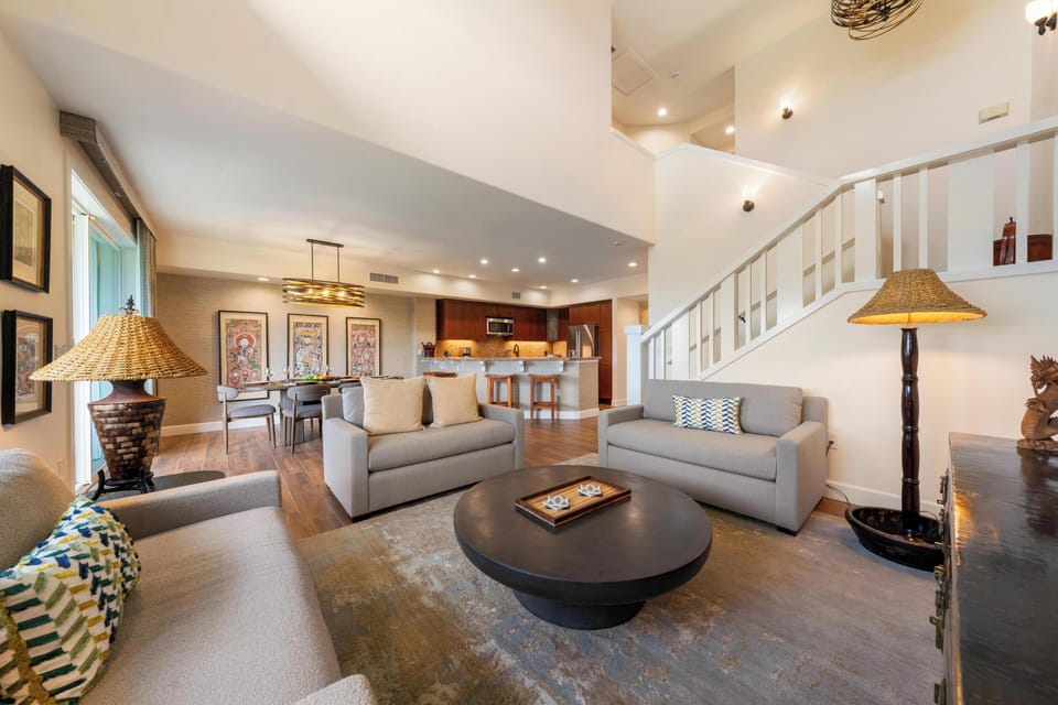Unwind in your spacious living area with plush sofas, warm lighting, and an open layout flowing into the modern kitchen.