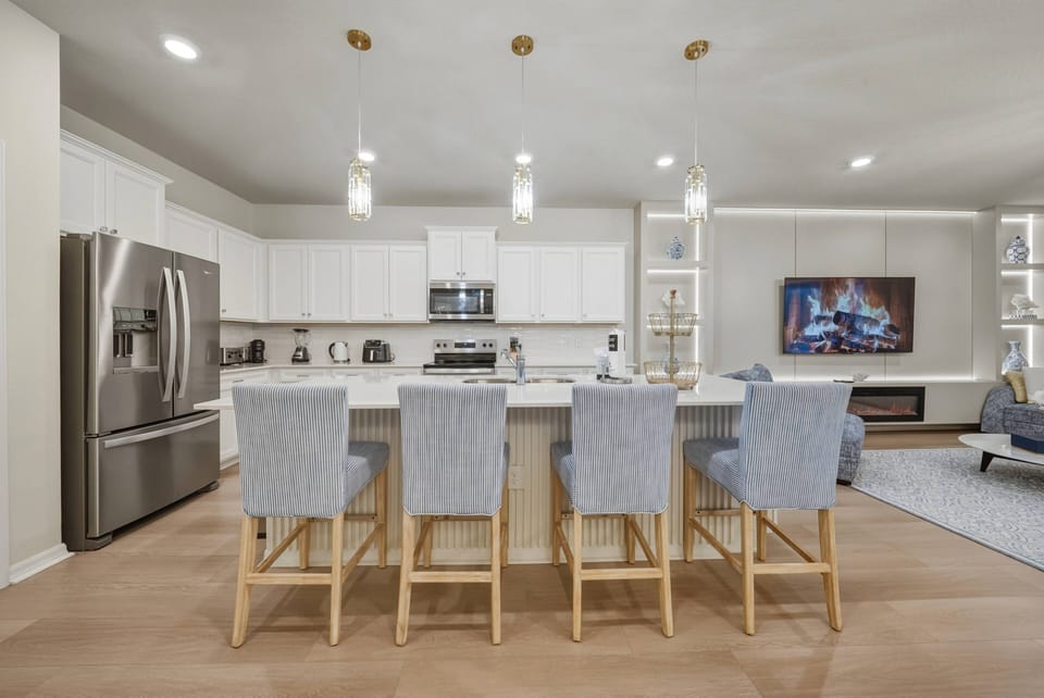 This bright and airy kitchen features sleek white cabinetry paired with soft blue-striped bar stools that invite casual gatherings. Enjoy the modern appliances and stylish pendant lighting that enhance the warm, open layout.