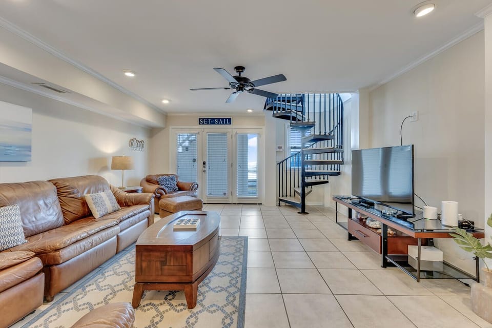 Unwind in this airy living room with plush leather seating and nautical touches, where your vacation stories unfold beneath the gentle breeze of ceiling fans.