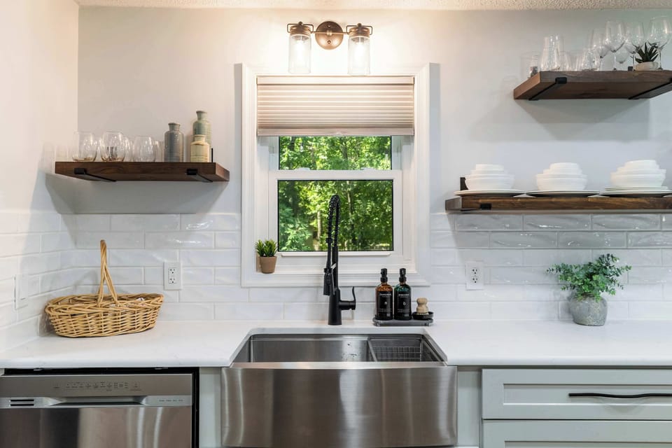 A designer farmhouse sink with a forest window view, open walnut shelving, and a full dishwasher — the details that make this Pocono kitchen one of the best in the area.