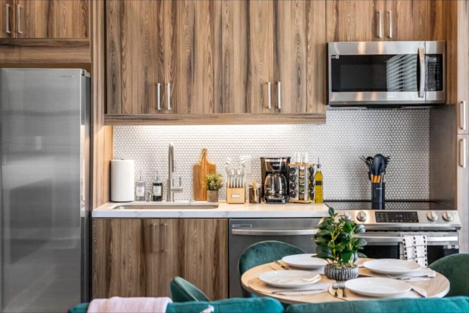 Full Modern Kitchen: Features sleek light-wood cabinetry, granite countertops, and premium stainless steel appliances, including a refrigerator, dishwasher, oven, and microwave.