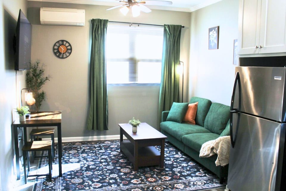 Living Area. Featuring a plush green sofa, a dedicated workspace/dining table, and a large flat-screen TV.