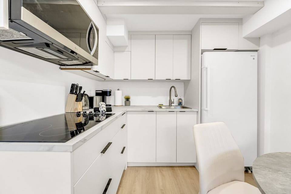 Close-up view of the fully-equipped, sleek white kitchen featuring modern cabinetry, contrasting black countertops, and essential cooking tools.