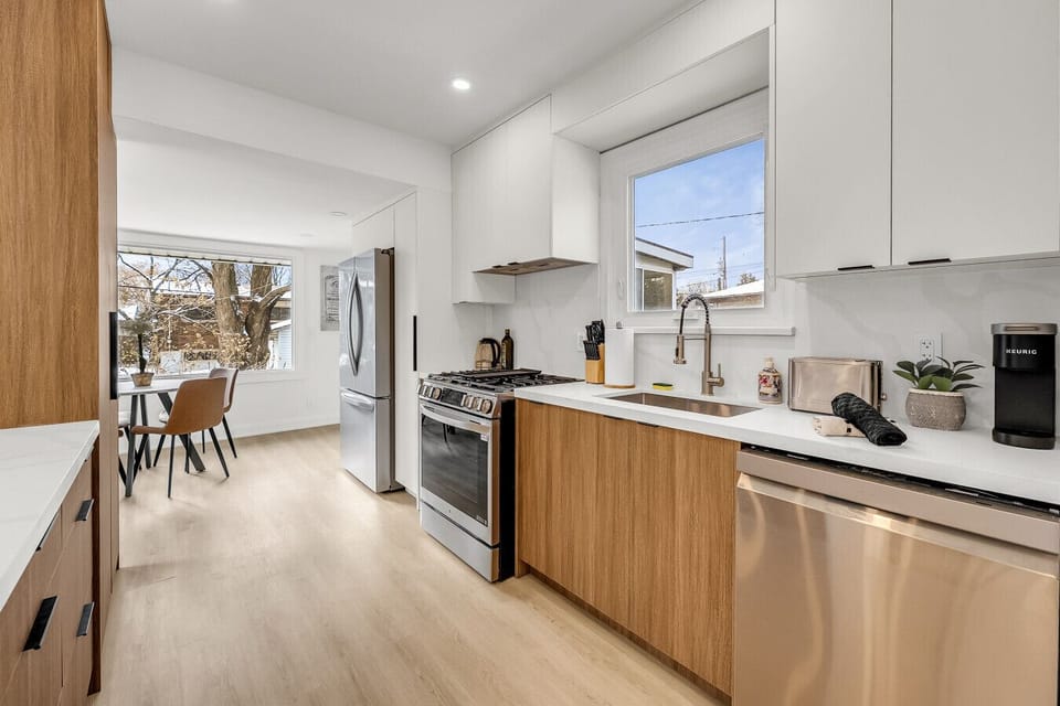 Fully equipped kitchen showcasing warm wood lower cabinets, clean white upper cabinets, stainless steel appliances, and a compact dining nook by the window.