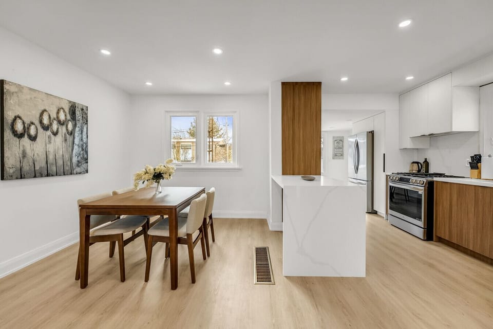 Modern dining area with seating for six, perfectly situated next to the kitchen island. Notice the warm wood cabinetry blending seamlessly with the white walls.