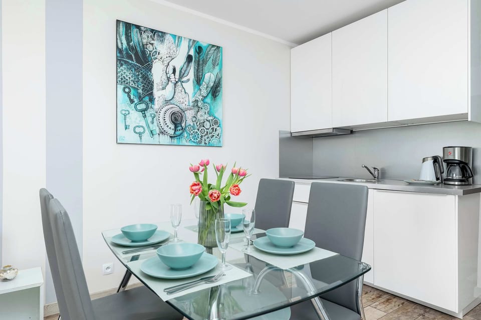 A compact kitchen and dining setup with white cabinetry and turquoise dishware. The decor feels fresh and modern with soft lighting.