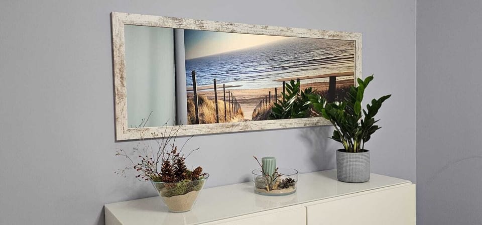 A bright vanity area decorated with small potted plants and a large scenic wall print depicting a coastal view. Clean white surfaces create a fresh, modern atmosphere.