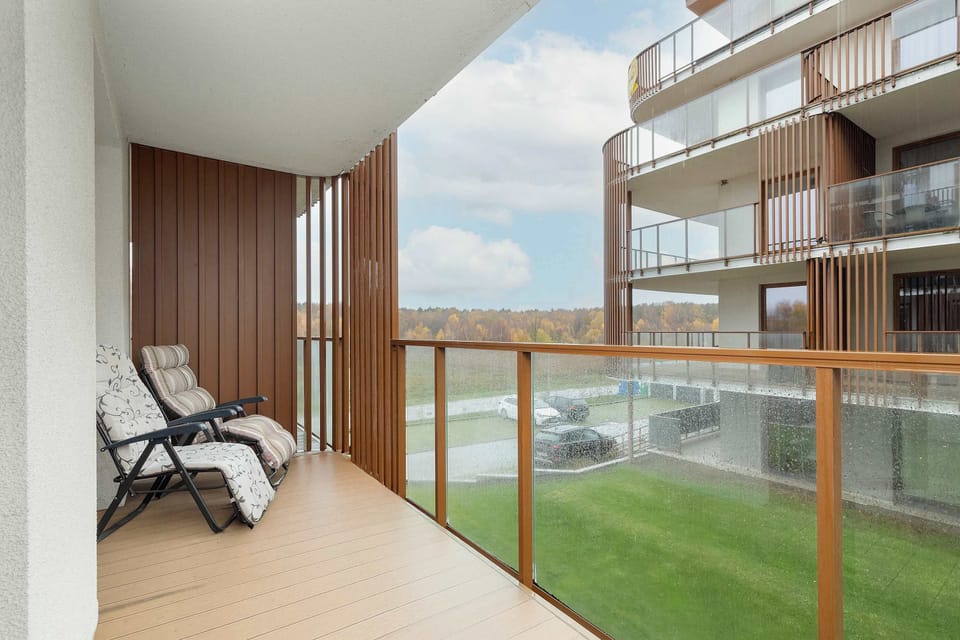 A balcony area with a small table and chairs overlooking modern apartment buildings. Wood and glass elements create a warm outdoor retreat.