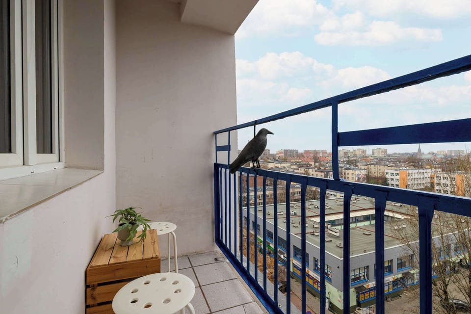Balcony with a blue railing overlooking trees and nearby buildings.