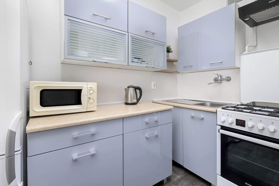 Compact kitchen with light cabinets, microwave, kettle, and stove arranged along one wall.