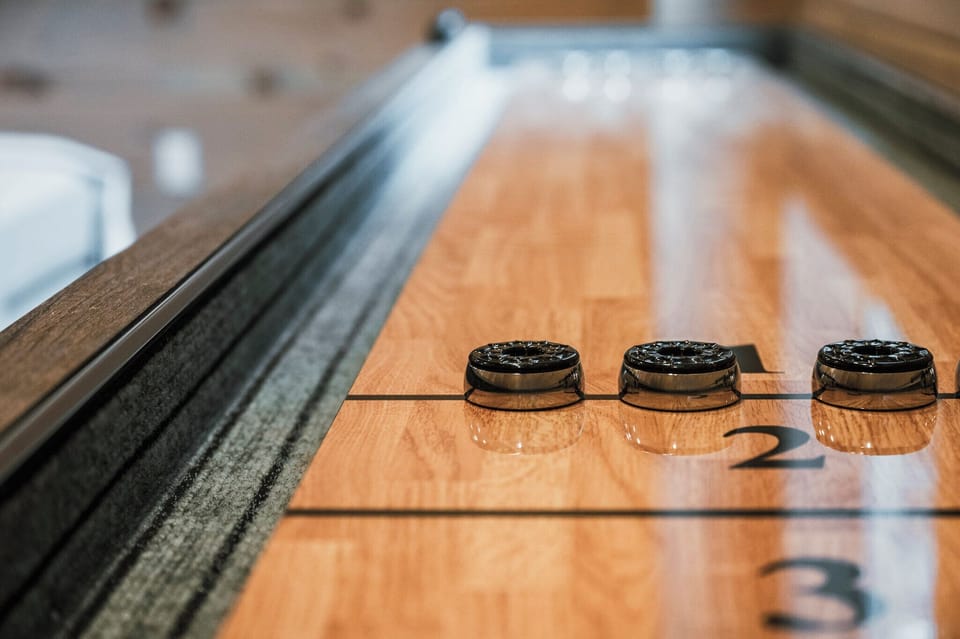 A shuffleboard table stands ready, its surface smooth and polished. Pucks are lined up, inviting a friendly game in a cozy setting