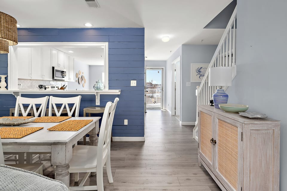 4306 Pettinaro Drive, Bethany Bay - Ocean View - kitchen transit - Bright dining area featuring a white wooden table set and a glimpse into the modern kitchen with blue accent walls.