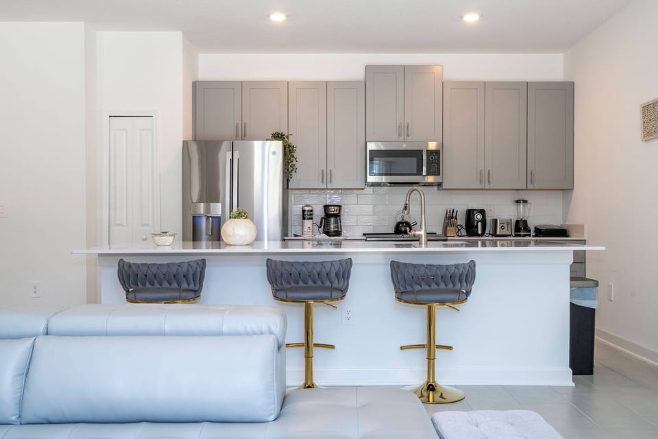 This stylish kitchen combines gray cabinetry with a bright white countertop for a fresh, functional space. The gold-accented bar stools invite casual dining, and modern appliances make meal prep a breeze for your comfort.