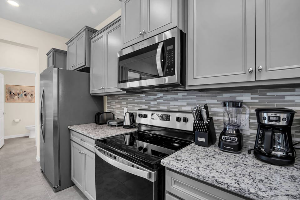 Experience culinary adventures in this well-equipped kitchen featuring sleek gray cabinetry, sparkling granite countertops, and modern appliances, all highlighted by a stylish mosaic backsplash for memorable meals.
