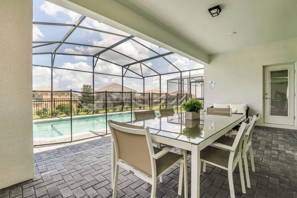 Step outside to discover a delightful dining area under a screened patio, where a sleek table and comfortable chairs invite alfresco meals. Enjoy the view of the shimmering pool and lush surroundings, perfect for relaxation.