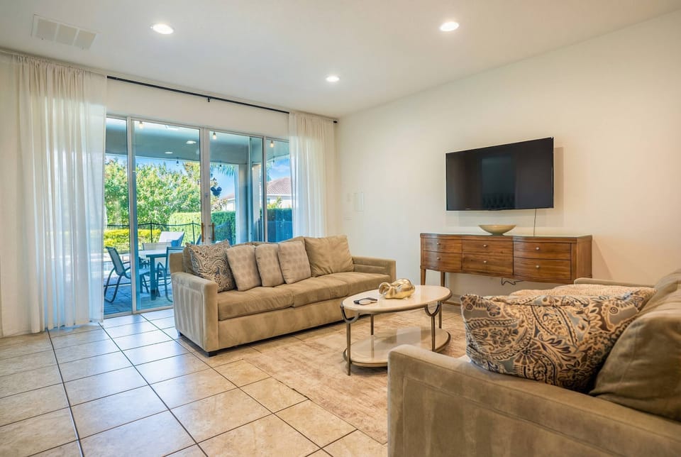 Bright and airy, this living room features soft beige sofas that invite relaxation, complemented by a stylish coffee table. Large sliding glass doors let in natural light and provide a seamless connection to the outdoor patio.