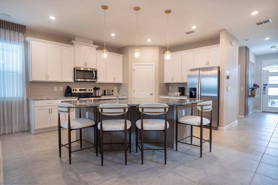 Step into a beautifully designed kitchen where sleek white cabinetry meets stylish fixtures. The spacious island, surrounded by chic bar stools, invites gatherings, while ample natural light enhances the welcoming atmosphere.