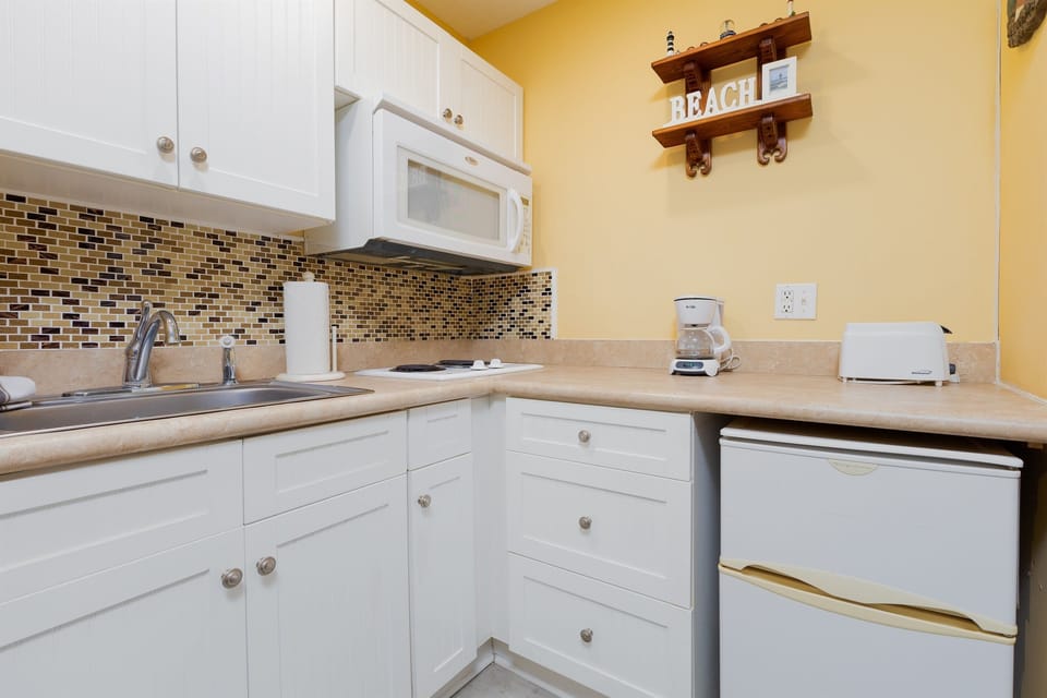 Compact kitchenette equipped with a mini fridge, microwave, coffee maker, toaster, and essentials for easy meals during your beach stay