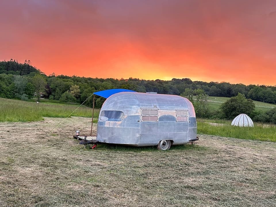 Vintage silver trailer glowing under a fiery countryside sunset.