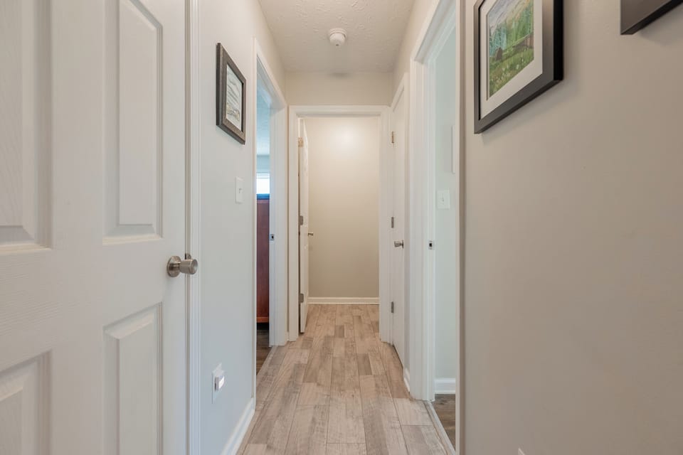Bright, welcoming hallway with wood-style floors and framed art—connecting bedrooms with warmth and charm.