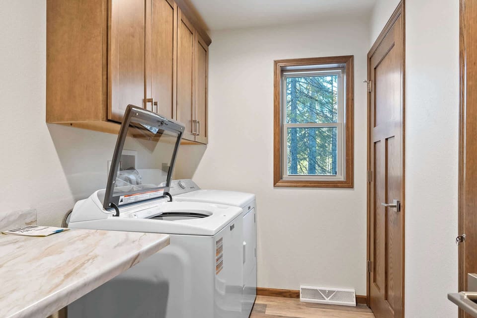 Your dedicated laundry space features modern machines and ample cabinet storage, with peaceful forest views while you tackle daily tasks.